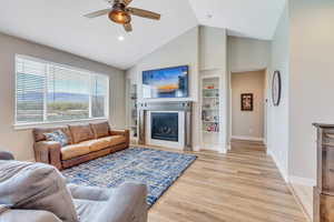 Living area featuring a ceiling fan, a glass covered fireplace, built in features, light wood finished floors, and baseboards