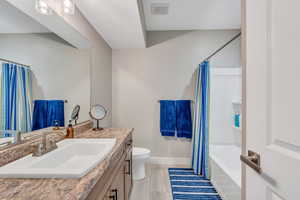 Full bathroom featuring baseboards, vanity, shower / bathtub combination with curtain, and toilet