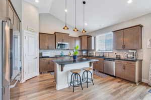 Kitchen with dark countertops, a sink, a breakfast bar, light wood-type flooring, and appliances with stainless steel finishes