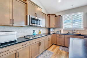 Kitchen with dark countertops, vaulted ceiling, a sink, light wood-style flooring, and appliances with stainless steel finishes
