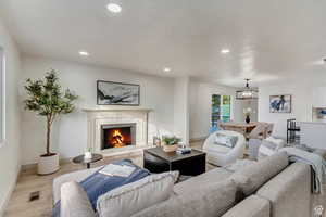 Living area featuring light wood-type flooring, a premium fireplace, recessed lighting, and an inviting chandelier