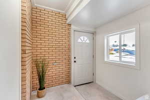 Entrance foyer with brick wall, baseboards, and light tile patterned floors