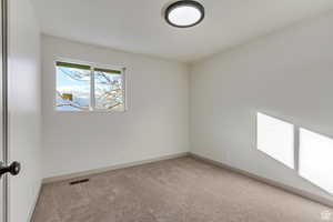 Spare room featuring visible vents, light carpet, and baseboards