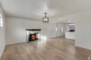 Unfurnished living room with baseboards, a lit fireplace, a chandelier, and light wood-style floors