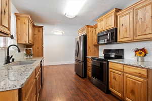 Kitchen with tasteful backsplash, a textured ceiling, a sink, stainless steel appliances, and baseboards
