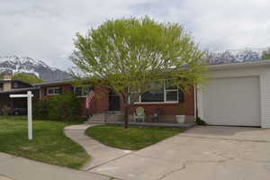 Single story home with a mountain view, concrete driveway, a garage, brick siding, and a front yard