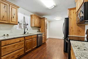 Kitchen featuring tasteful backsplash, a textured ceiling, a sink, stainless steel appliances, and baseboards