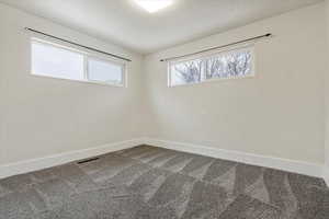 Empty room featuring visible vents, dark colored carpet, and baseboards