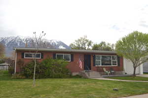 Single story home featuring a front lawn, brick siding, a mountain view, and a garage