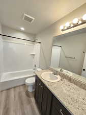 Bathroom with a textured ceiling, wood finished floors, visible vents, and shower / bathing tub combination