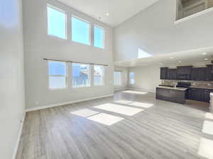 Unfurnished living room featuring high vaulted ceiling, baseboards, light wood finished floors, and a wealth of natural light