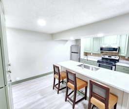 Kitchen featuring a textured ceiling, a breakfast bar area, stainless steel appliances, and a sink