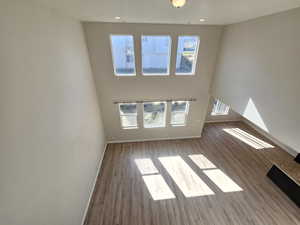 Unfurnished living room featuring recessed lighting, wood finished floors, a towering ceiling, and baseboards