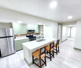 Kitchen with a sink, light wood-type flooring, green cabinets, stainless steel appliances, and a kitchen bar