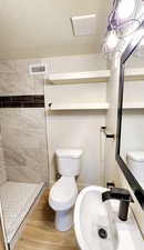 Full bathroom with a sink, toilet, a tile shower, visible vents, and wood finished floors