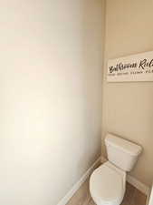 Bathroom featuring wood finished floors, toilet, and baseboards