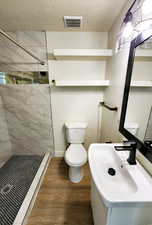 Full bathroom featuring toilet, wood finished floors, visible vents, and tiled shower