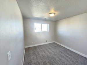 Carpeted empty room featuring baseboards, a textured ceiling, and visible vents
