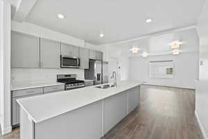 Kitchen with light wood finished floors, a sink, a large island, gray cabinets, and appliances with stainless steel finishes