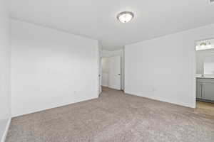 Unfurnished bedroom featuring ensuite bath, light carpet, a sink, and baseboards