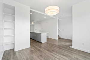 Unfurnished living room with a sink, visible vents, baseboards, wood finished floors, and stairs