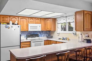 Kitchen featuring a kitchen breakfast bar, light countertops, a sink, white appliances, and a peninsula