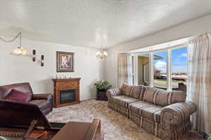 Living room with a fireplace, a chandelier, a textured ceiling, and carpet