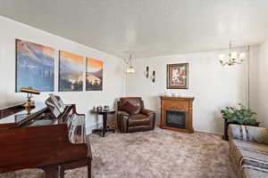Living area featuring a textured ceiling, carpet, an inviting chandelier, a fireplace, and baseboards