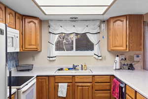 Kitchen featuring brown cabinetry, a sink, white appliances, and light countertops