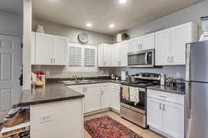 Kitchen featuring dark countertops, a sink, stainless steel appliances, a peninsula, and recessed lighting