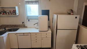Kitchen featuring white cabinets, a sink, white appliances, and light countertops