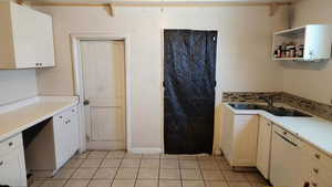 Kitchen featuring tasteful backsplash, white dishwasher, a sink, light tile patterned floors, and light countertops