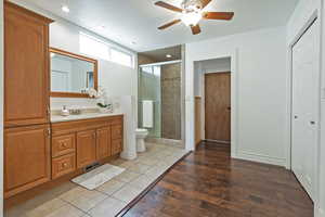 Full bathroom featuring toilet, vanity, a ceiling fan, wood-type flooring, and a stall shower