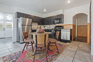Kitchen with a wainscoted wall, light countertops, light tile patterned floors, arched walkways, and black appliances