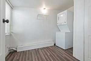 Washroom featuring stacked washer / drying machine, wood finished floors, visible vents, and laundry area