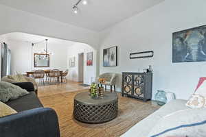 Living room featuring light wood finished floors, rail lighting, arched walkways, baseboards, and a chandelier