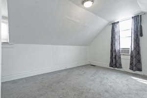 Additional living space with a textured ceiling, a textured wall, baseboards, lofted ceiling, and carpet flooring