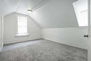 Additional living space featuring baseboards, vaulted ceiling, carpet flooring, and a textured ceiling
