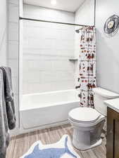 Bathroom featuring wood tiled floor, shower / bath combo with shower curtain, toilet, and vanity