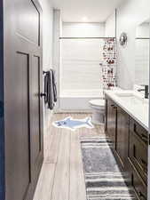 Full bathroom with vanity, wood finished floors, shower / bathtub combination with curtain, and toilet