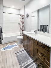 Bathroom with toilet, visible vents, wood finished floors, shower / bathtub combination with curtain, and vanity