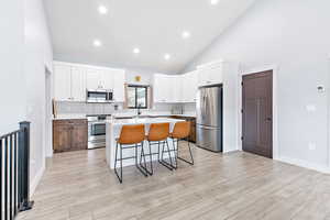 Kitchen with a breakfast bar, a center island, light countertops, white cabinets, and stainless steel appliances