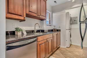 Kitchen featuring stainless steel appliances, a sink, estacked washer and dryer, dark stone countertops, and brown cabinets