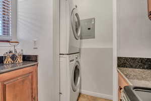 Washroom featuring stacked washing machine and dryer, electric panel, light tile patterned floors, and baseboards