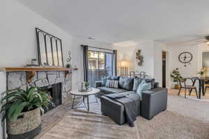 Living area with a ceiling fan, a stone fireplace, and carpet