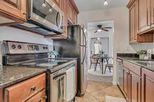 Kitchen with stainless steel appliances, ceiling fan, a sink, light tile patterned floors, and brown cabinetry