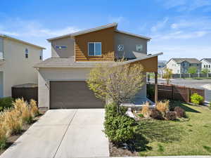 View of front of house with stucco siding, fence, an attached garage, concrete driveway, and a residential view