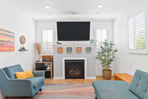 Living room with a wealth of natural light, a glass covered fireplace, baseboards, and wood finished floors
