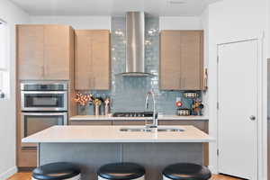 Kitchen with a sink, light countertops, wall chimney exhaust hood, and a kitchen bar
