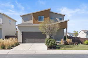 Modern home with concrete driveway, stucco siding, fence, and an attached garage